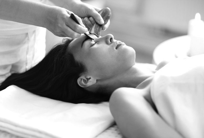 a masseuse giving a woman Gua Sha facial massage