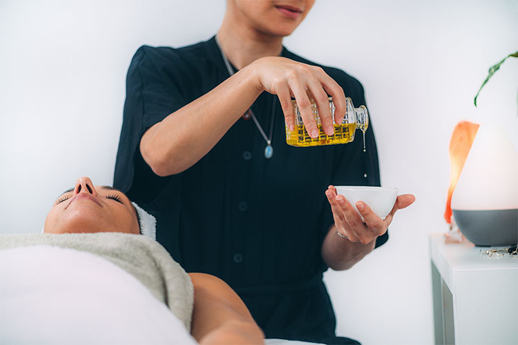 massage therapist pouring essential oils in a bowl for a massage on woman